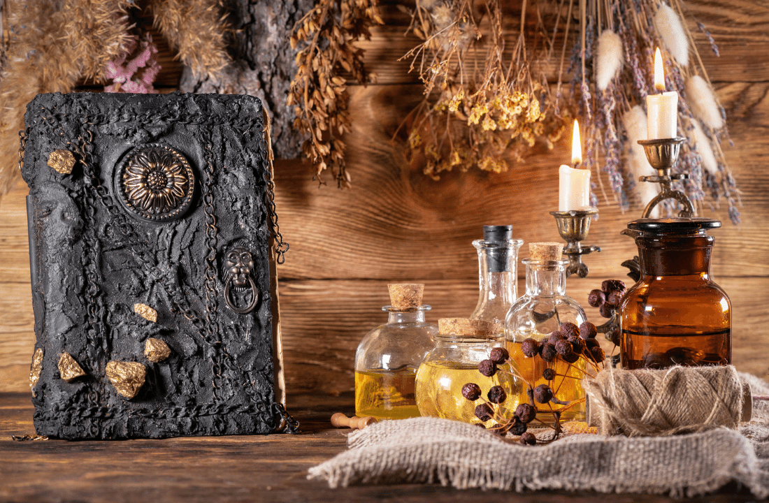IMAGE: another stunning altar that celebrates the elements: comeplete with an array of oils in bottles, dried flowers hung upside down, a candle that is nearly burned out and a handmade, black book of shadows with a faded golden sunflower at it's center. This altar is gently composed in front of a wall made of wood planks.